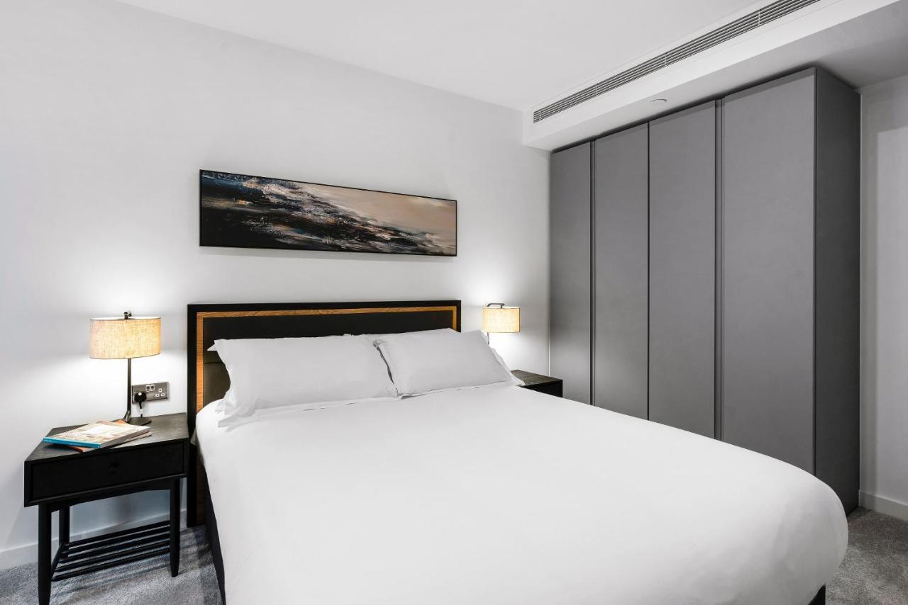 Citysuites 2 Aparthotel Manchester Exterior photo The photo shows a modern bedroom designed with a minimalist aesthetic. The focal point is a large bed with white bedding, positioned against a wall. On either side of the bed, there are black nightstands topped with lamps, providing a warm glow. Abov