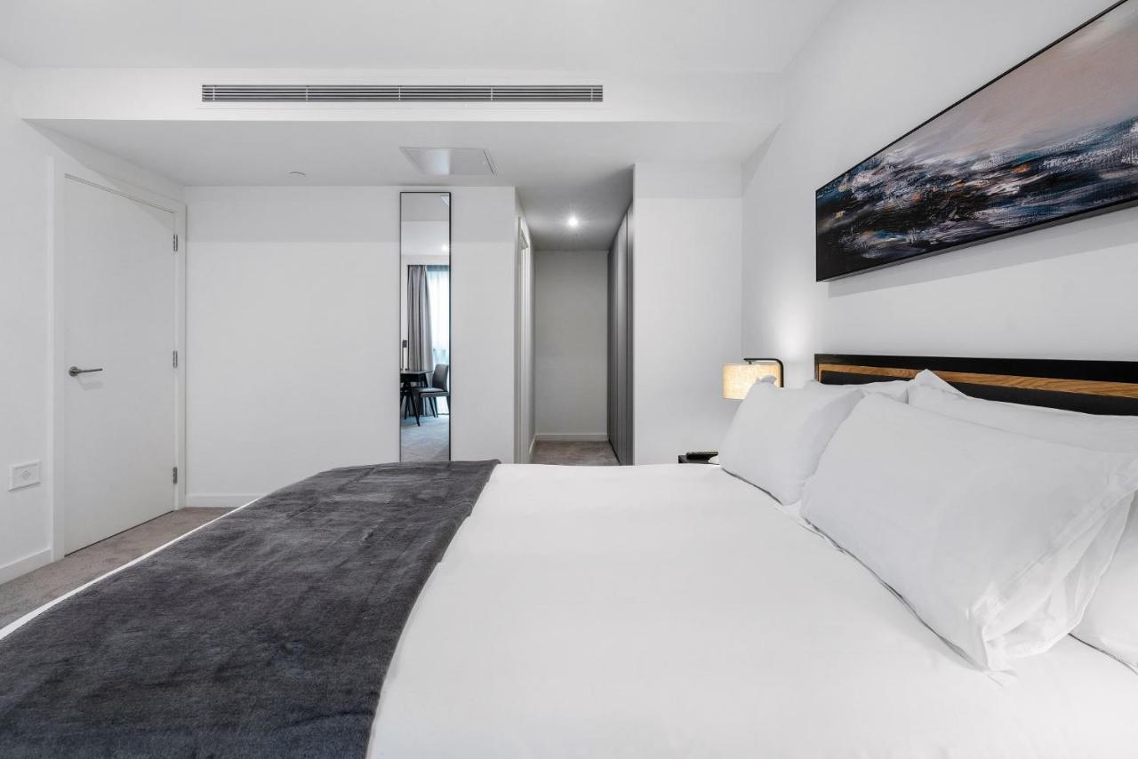 Citysuites 2 Aparthotel Manchester Exterior photo The photo shows a modern bedroom with a minimalistic design. In the foreground, there is a neatly made bed with white linens and a dark gray throw blanket. To the side, there is a bedside lamp and a piece of abstract artwork on the wall above the bed