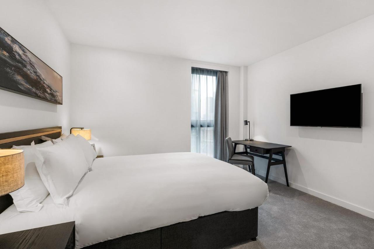 Citysuites 2 Aparthotel Manchester Exterior photo The photo shows a modern hotel room featuring a large bed with white linens and a dark headboard. There are two bedside lamps on either side of the bed. A desk with a chair is placed against one wall, and a flat-screen TV is mounted on another wall. 