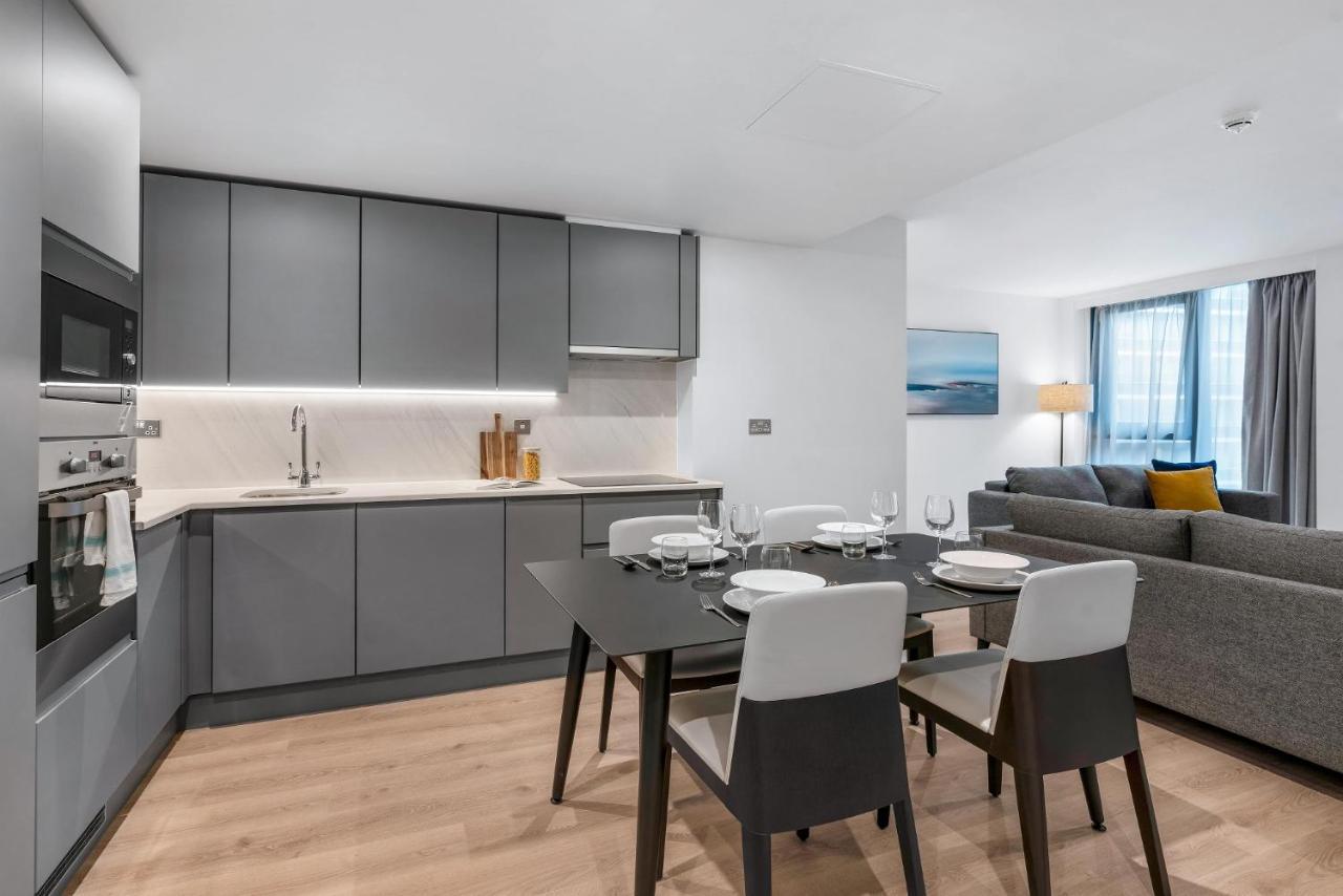 Citysuites 2 Aparthotel Manchester Exterior photo The photo shows a modern, open-concept kitchen and living area. The kitchen features sleek, gray cabinetry with a countertop, a sink, and built-in appliances. There are cooking utensils displayed on the countertop. Next to the kitchen, there is a din