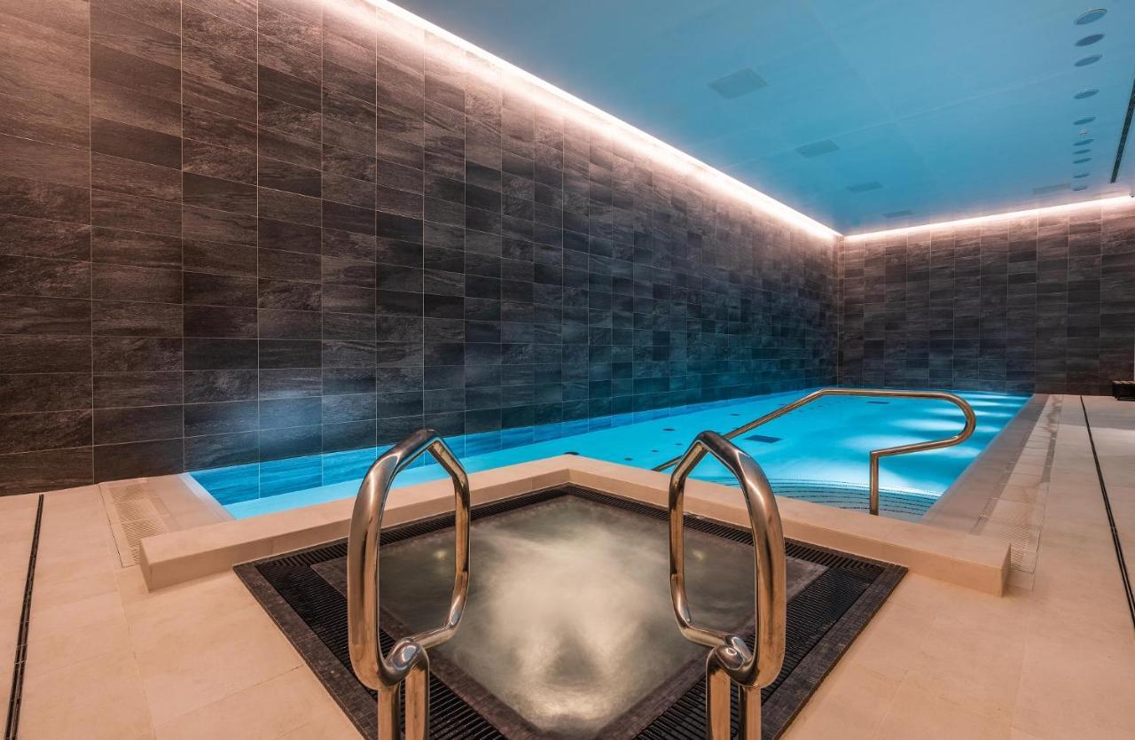 Citysuites 2 Aparthotel Manchester Exterior photo The photo shows a modern indoor swimming pool area. The pool features a sleek, rectangular design with a beautiful blue water that seems illuminated. Surrounding the pool are dark, textured walls, adding to the elegant atmosphere. There are dual meta