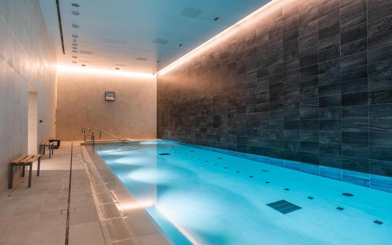 Citysuites 2 Aparthotel Manchester Exterior photo The photo shows an indoor swimming pool area. The pool is illuminated with a soft blue light, creating a calming atmosphere. The walls are designed with dark tiles, and there is a lighter tiled area surrounding the pool. Ambient lighting is installed