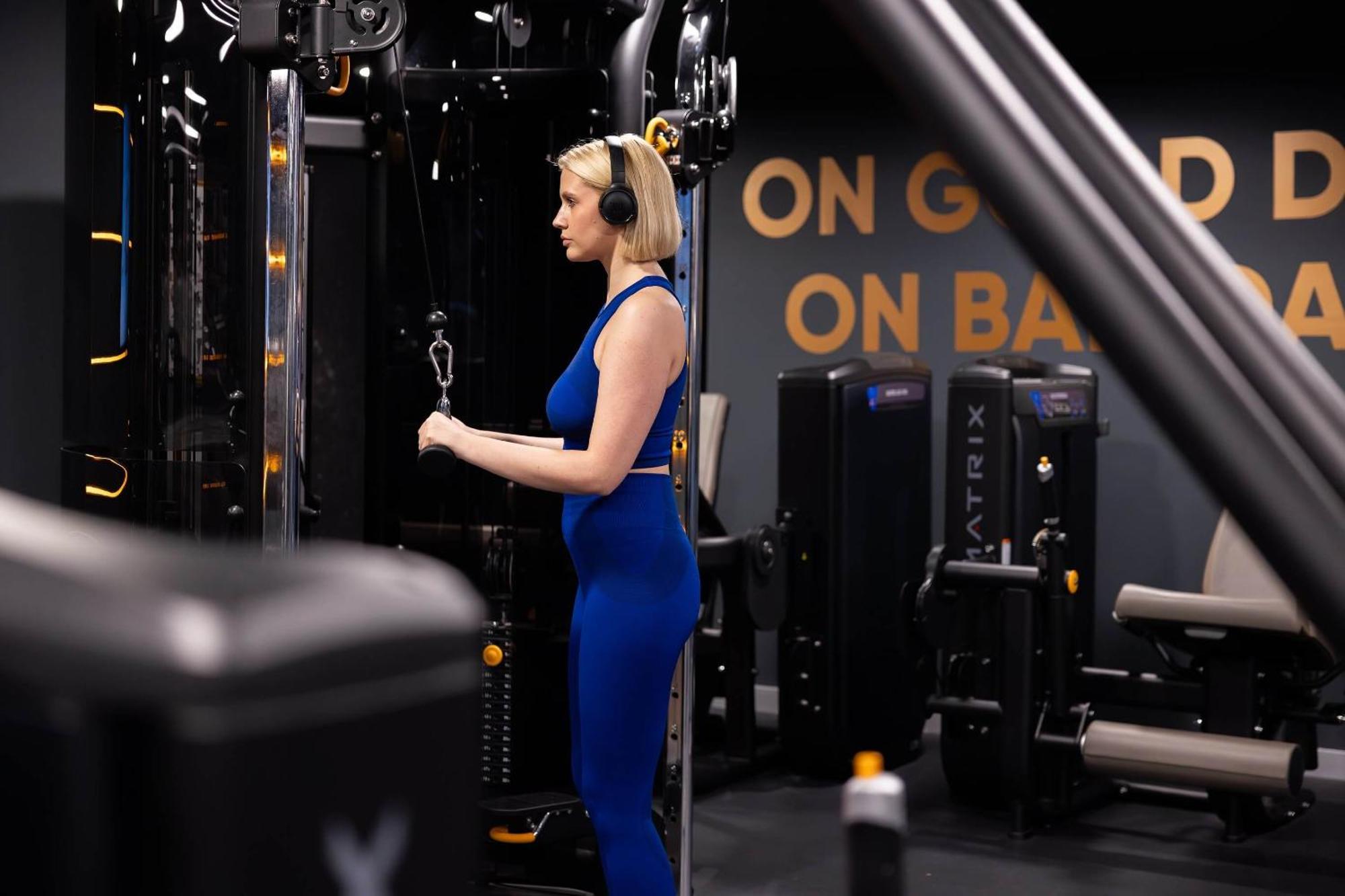 Citysuites 2 Aparthotel Manchester Exterior photo The photo shows a woman working out in a gym. She is wearing a blue athletic outfit and headphones while using a gym machine. The background features various other gym equipment and a wall with the words "ON GOOD ON BAD" displayed prominently. The se